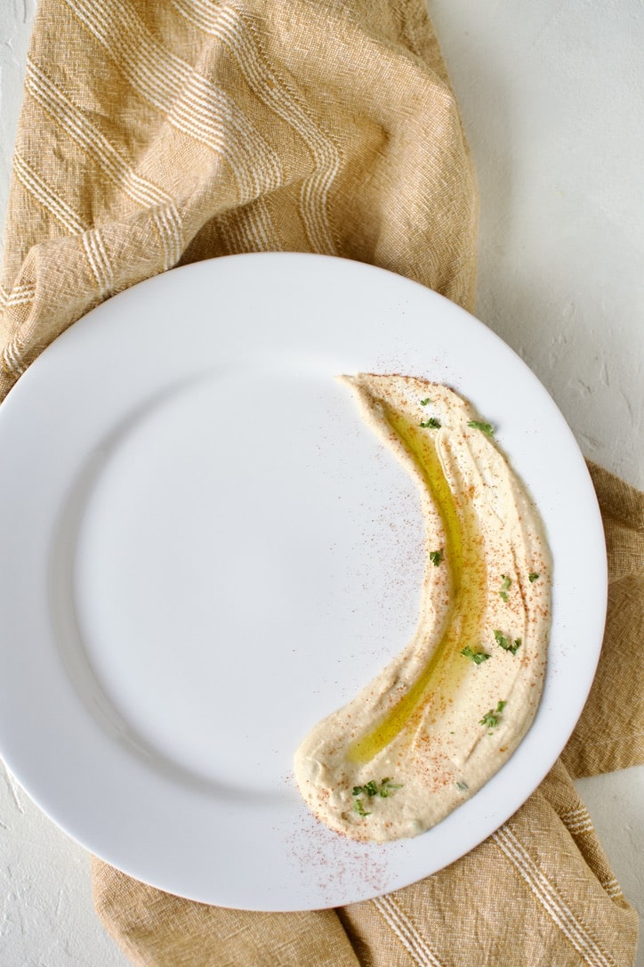 Assembling a plate of Greek Fries. Step 1, spread hummus on the bottom of the plate.