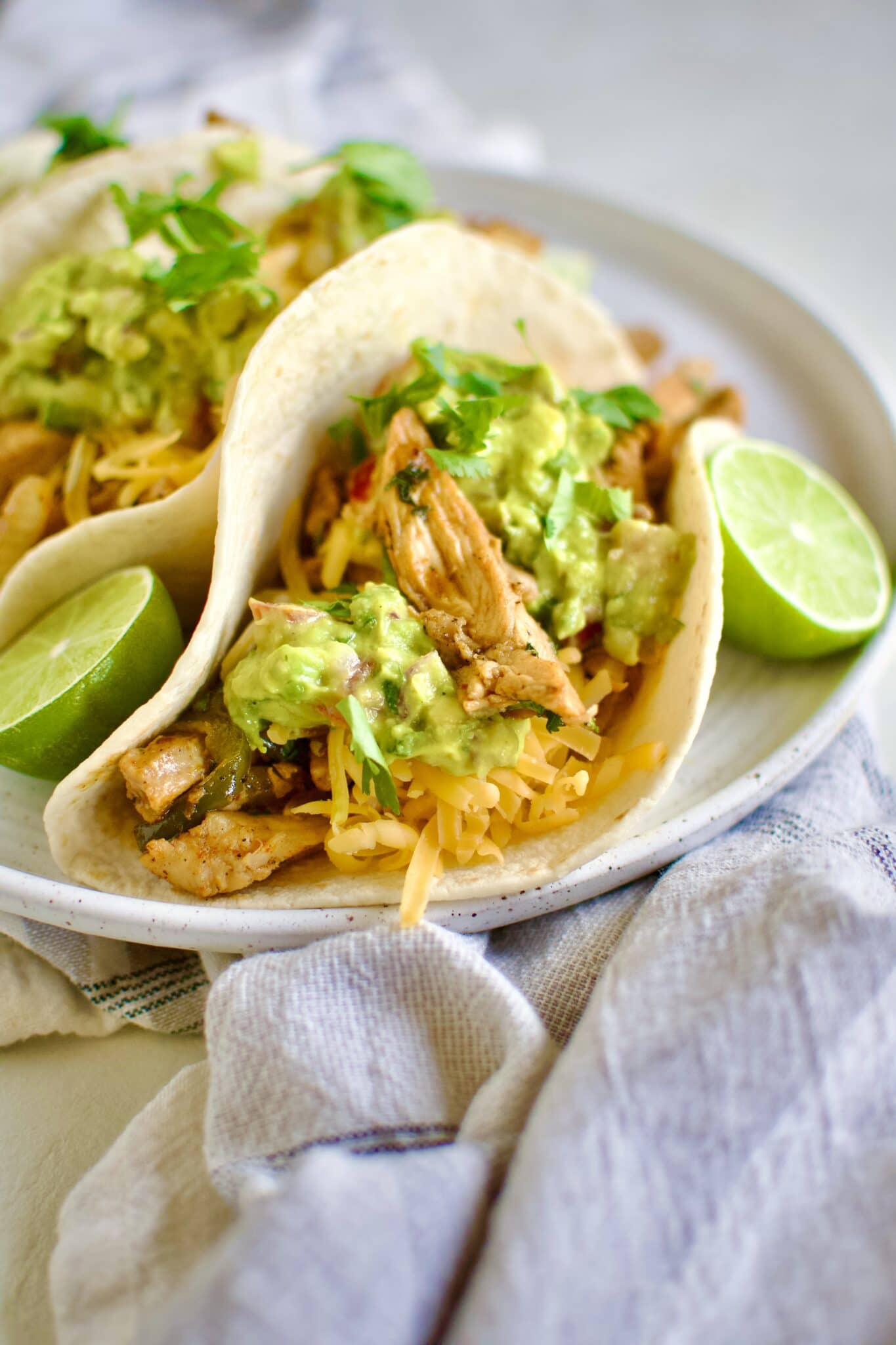 Easy Chicken Fajitas in tortillas topped with cheddar cheese, guacamole, and cilantro.