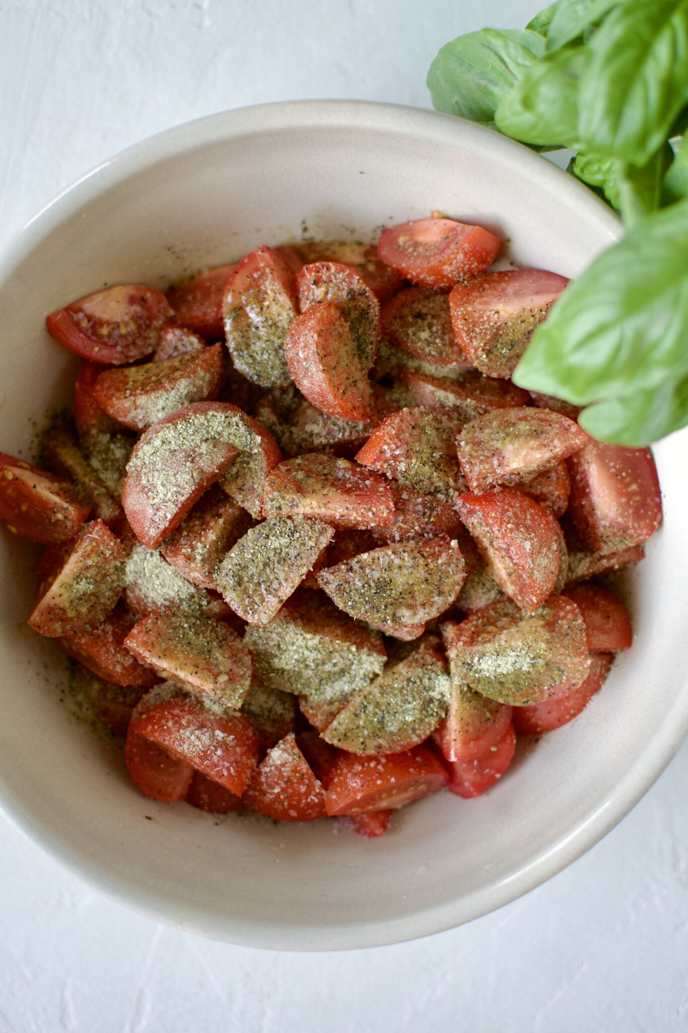 Seasoned tomatoes in a large bowl with olive oil, seasonings, vinegar.