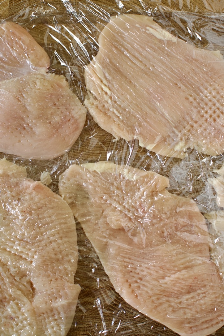 Tenderized Chicken breasts between plastic wrap.