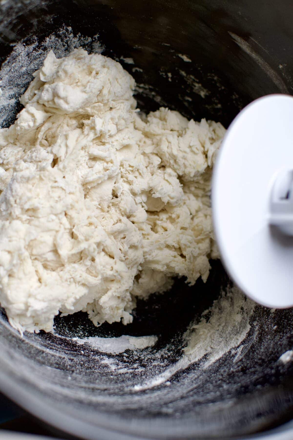 Making a shaggy dough by hand in the bowl of a stand mixer with the dough hook attachment before kneading with the machine.