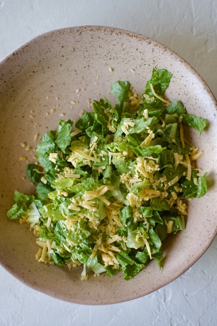 Lettuce in a bowl, topped with cheddar cheese.