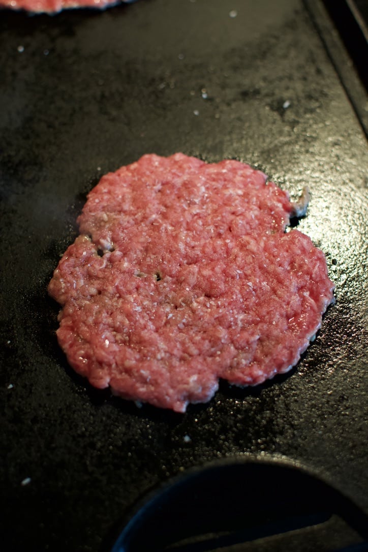 placing burger patty on a hot griddle.