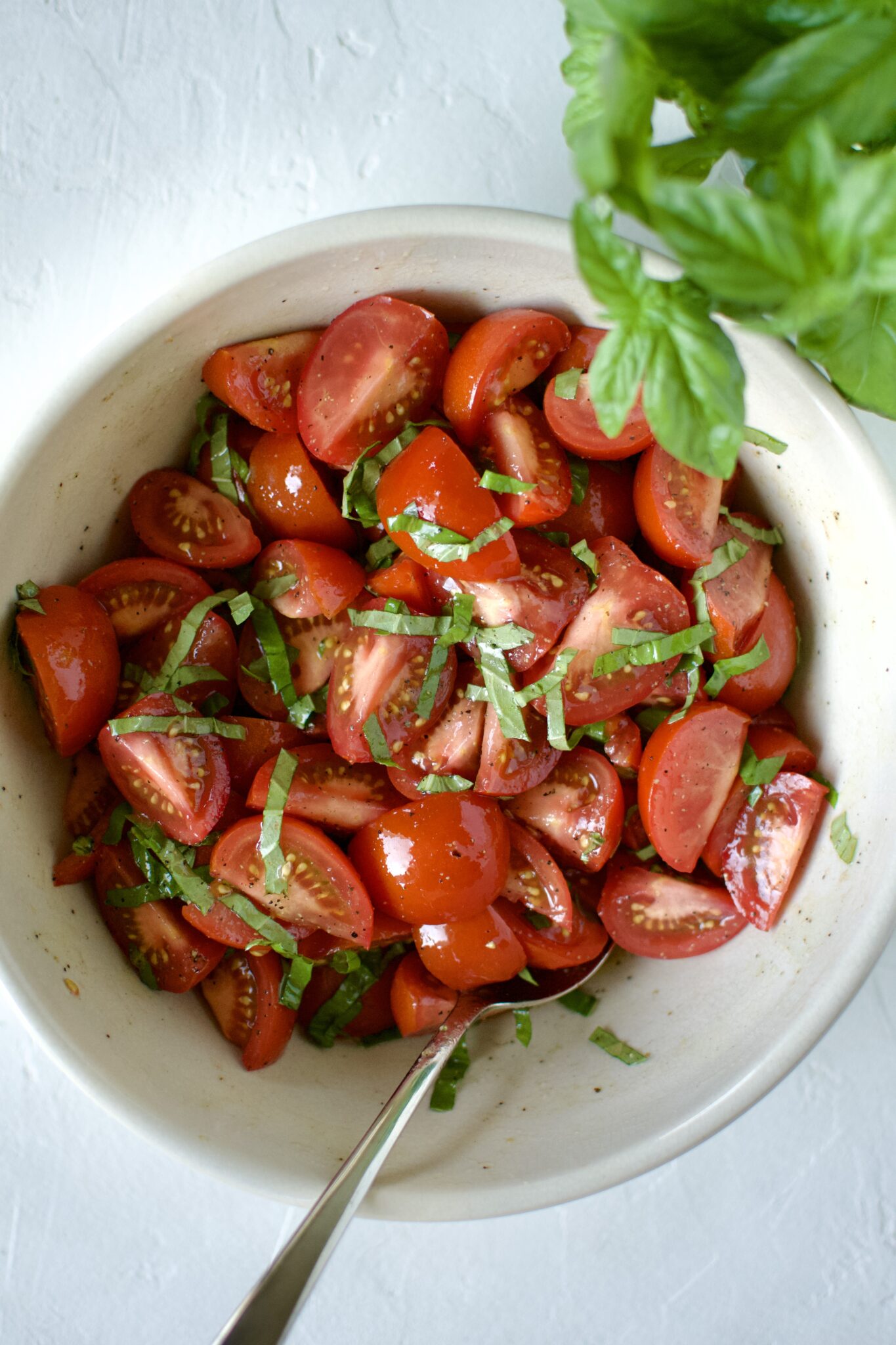 Seasoned tomatoes in a large bowl, tossed with olive oil, seasonings, vinegar, and basil strands.