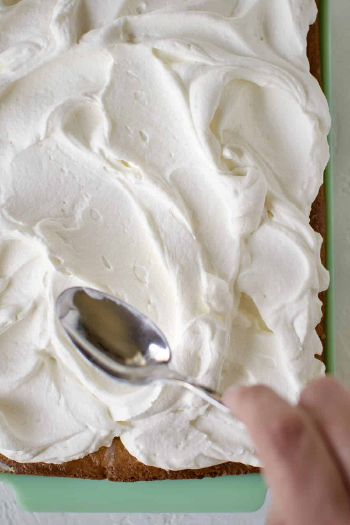 Spreading whipped cream over the tres leches cake.
