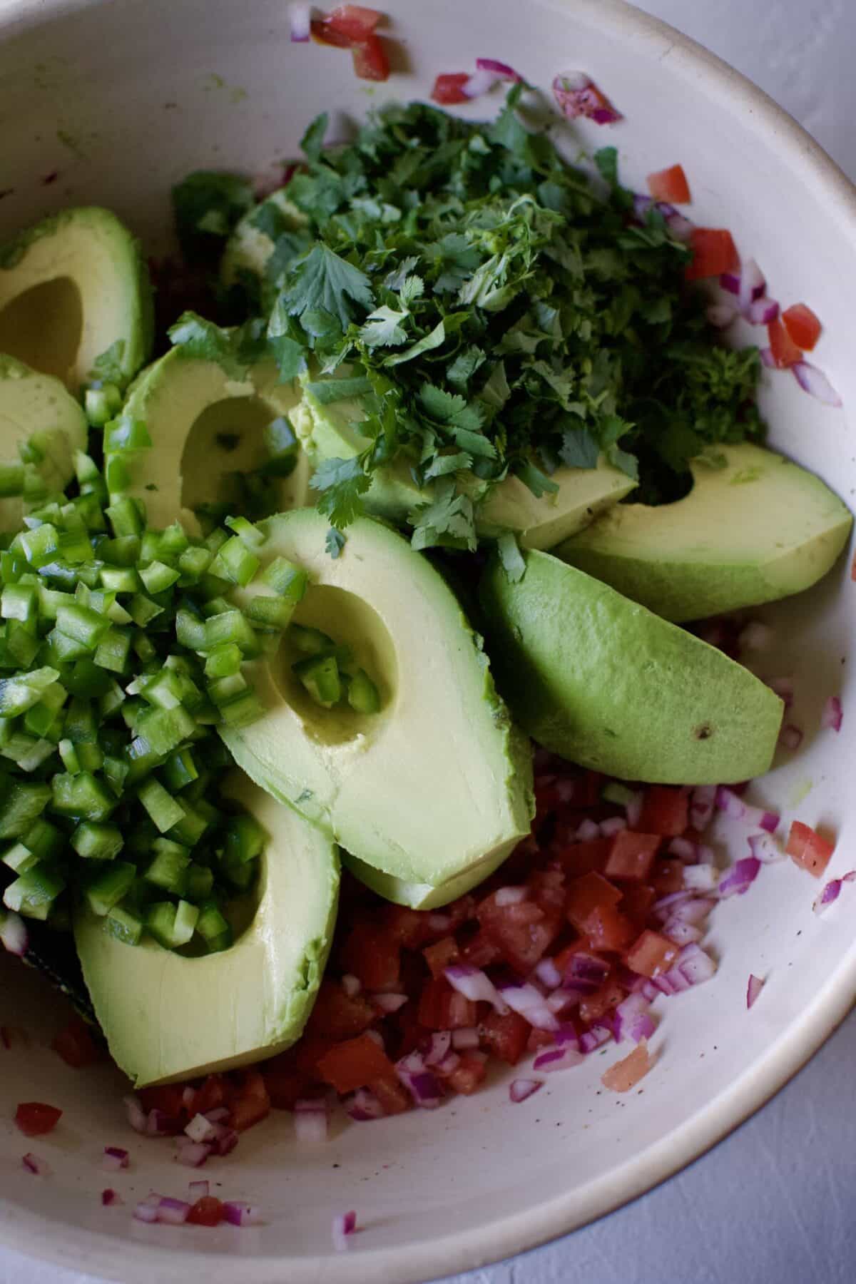 Avocado, jalapeno, and cilantro added to the bowl that has the onion, tomatoes, and lime juice already in it.