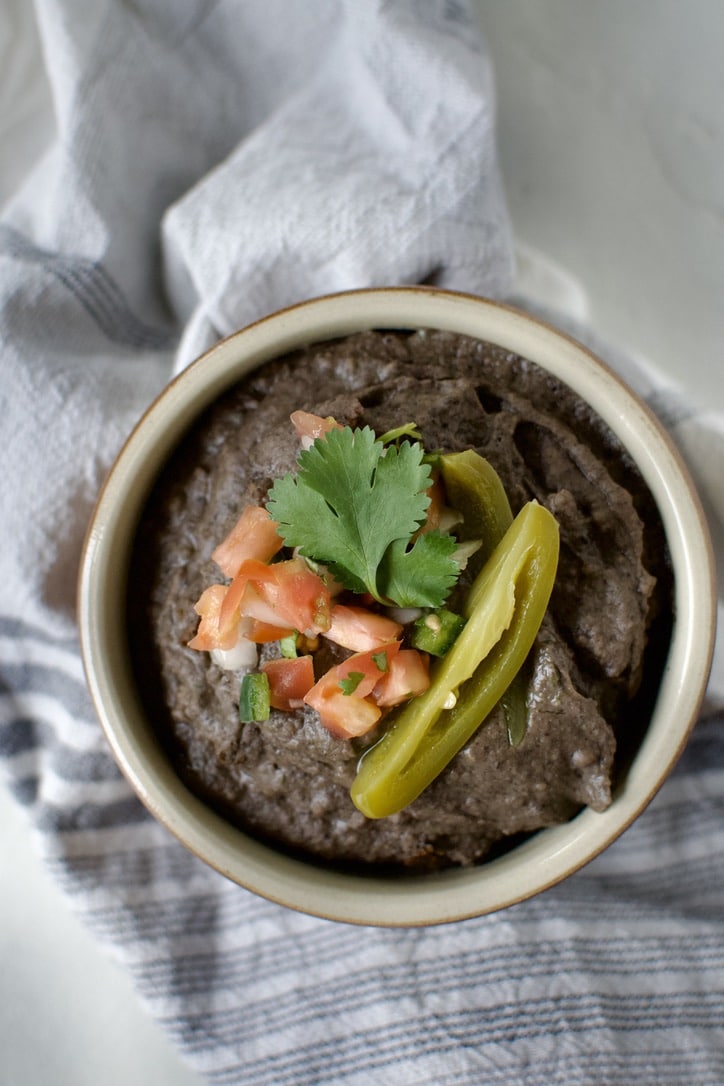 Black Bean Dip in a bowl, topped with pico de gallo, cilantro, and a slice of jalapeno.