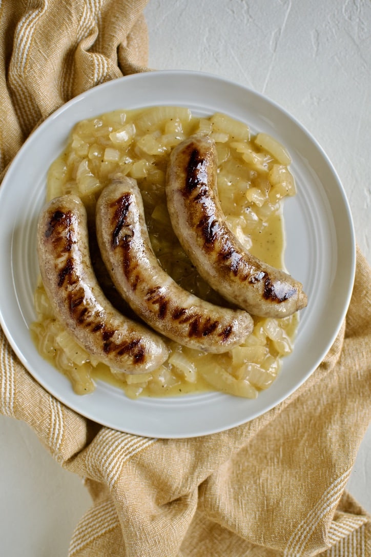 Braised and Grilled Brats served over braised and buttered onions.
