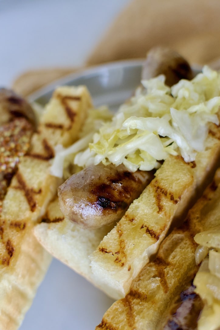 Braised and Grilled Brats served on grilled buns with sauerkraut on it.