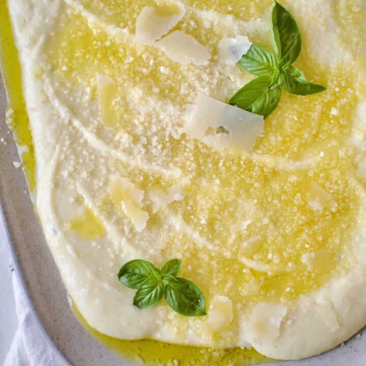 Creamy Polenta Recipe on a platter ready to eat. Topped with parmesan and basil.