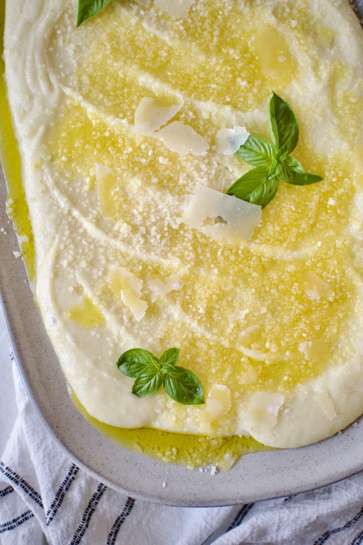 Creamy Polenta Recipe on a platter ready to eat. Topped with parmesan and basil.