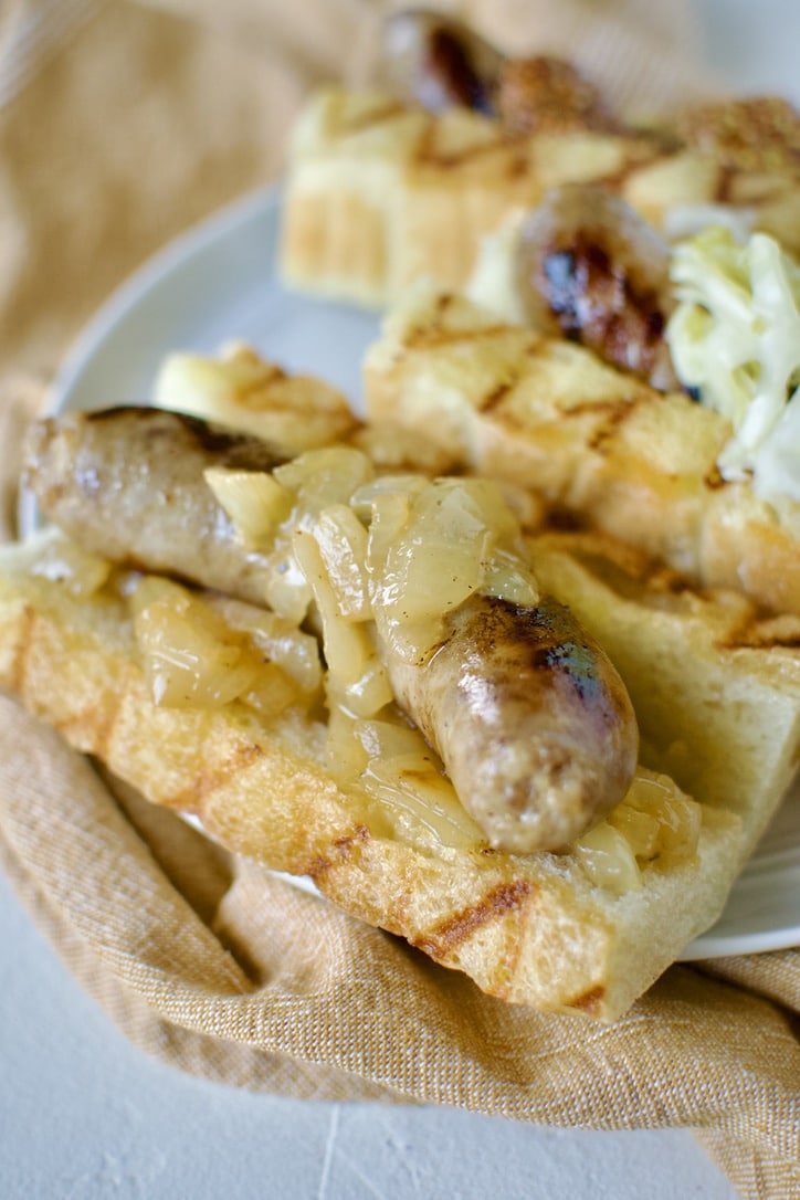 Braised and Grilled Brats served on grilled buns with onions on it.