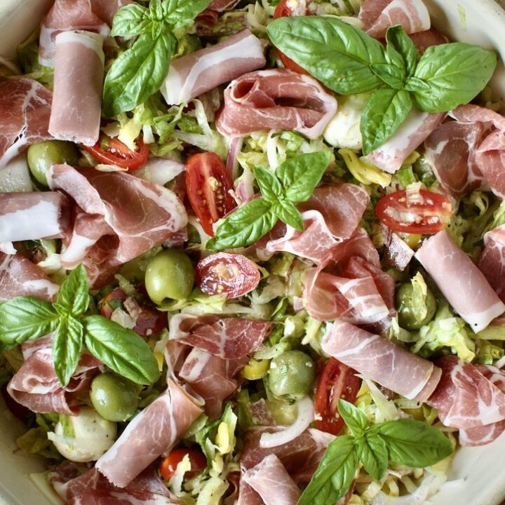 Mixed Italian Chopped Salad in a large bowl topped with prosciutto and basil leaves.