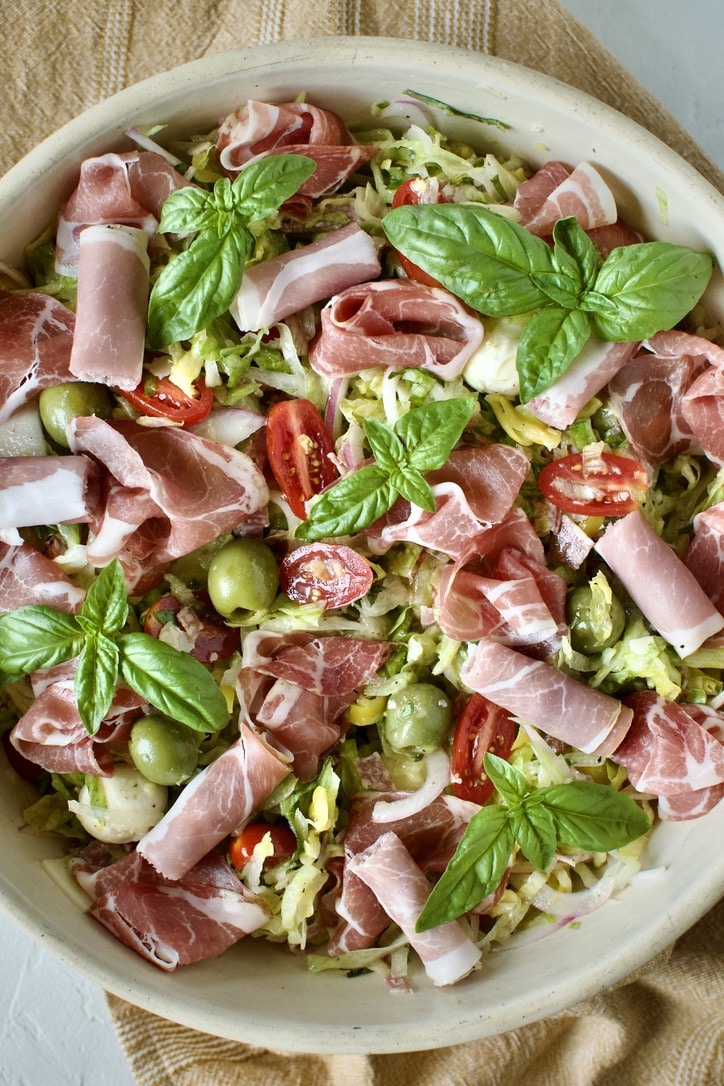 Mixed Italian Chopped Salad in a large bowl topped with prosciutto and basil leaves.