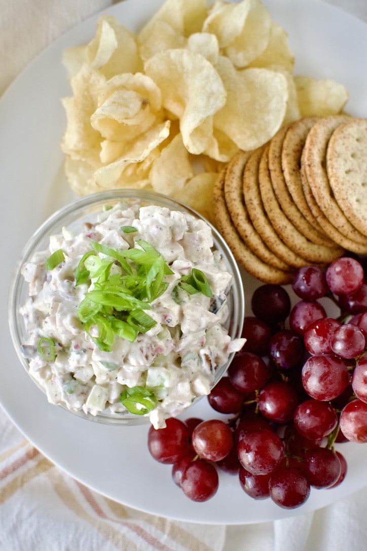 Chicken Salad in a cup on a plate with chips, crackers, and grapes.