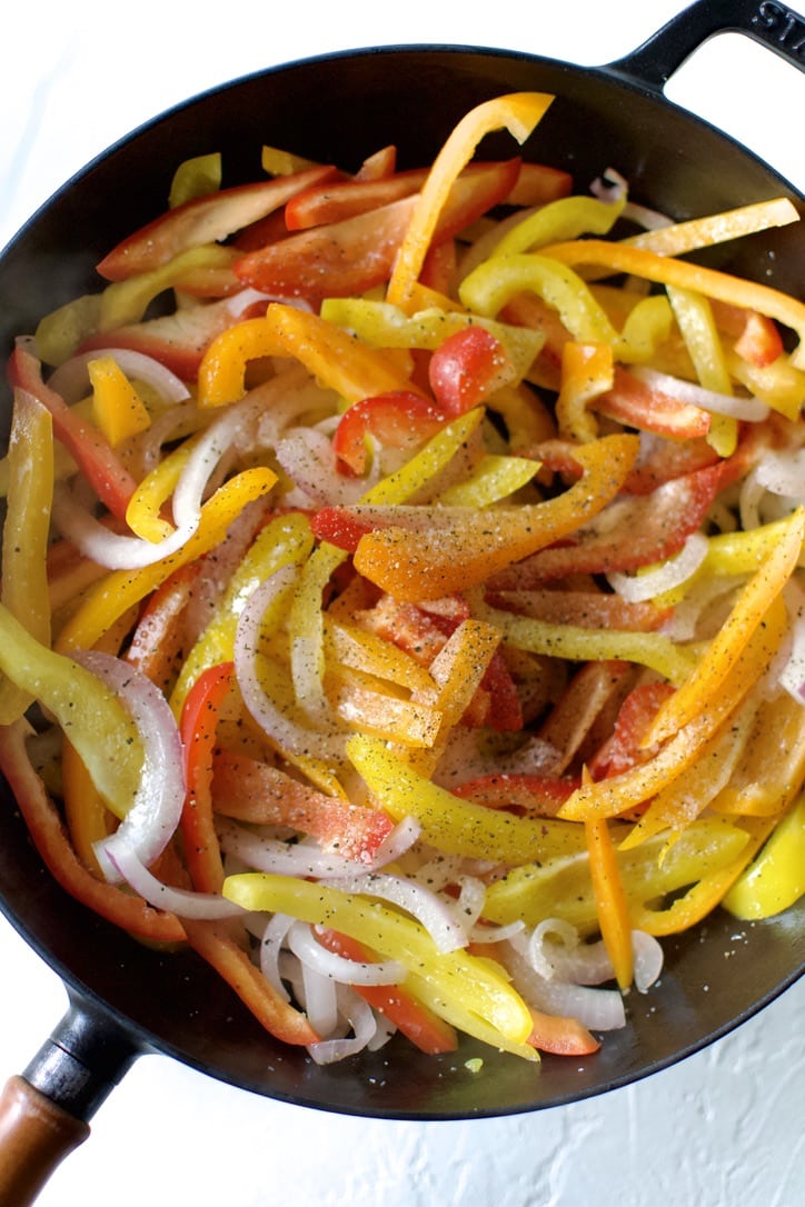 Adding onions and peppers to a hot pan.