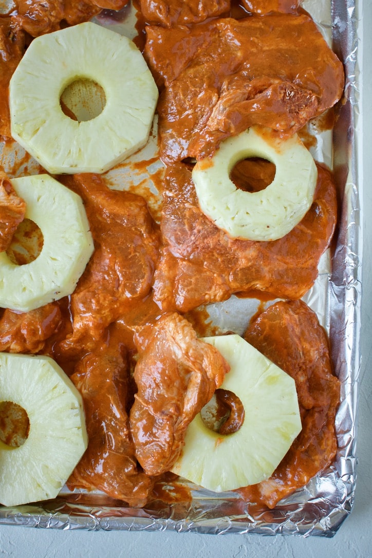 Marinated pork, and cut pineapple, on a sheet pan, before roasting.