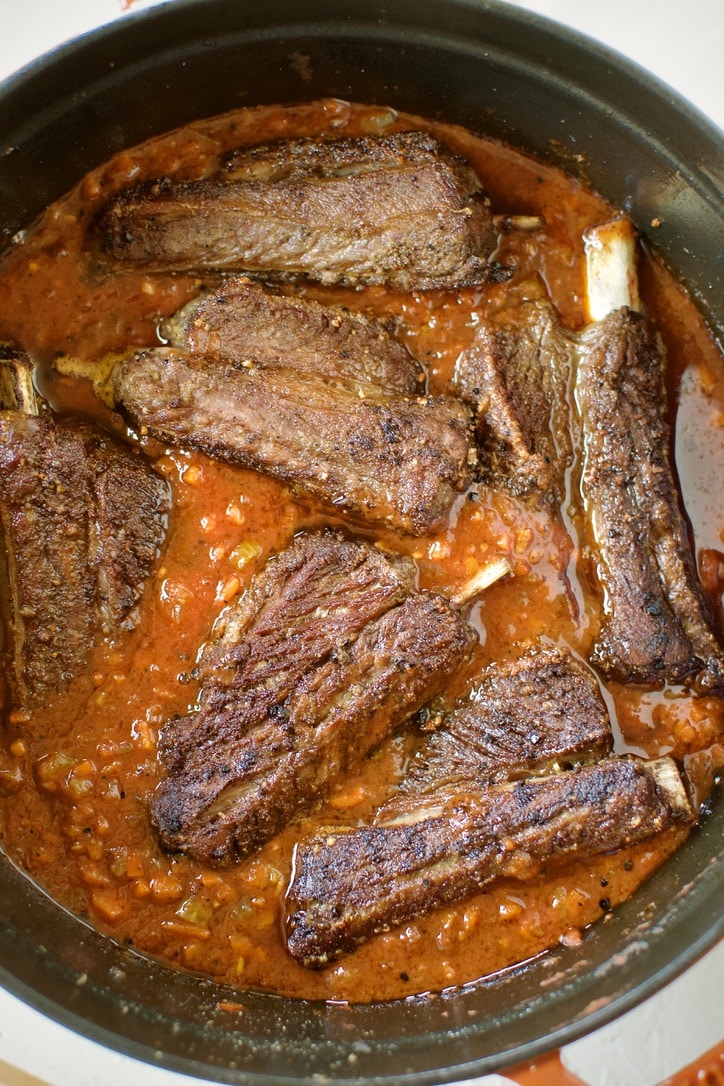 Seared short ribs nestled back into the pot that now has the sauce made in the bottom.