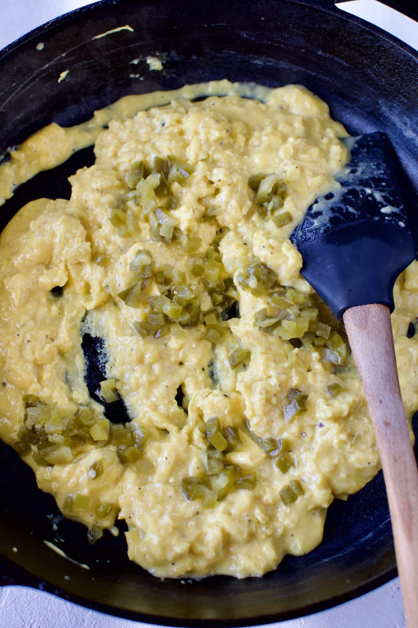 Scrambled eggs in a pan diced, pickle jalapeno being stirred in.