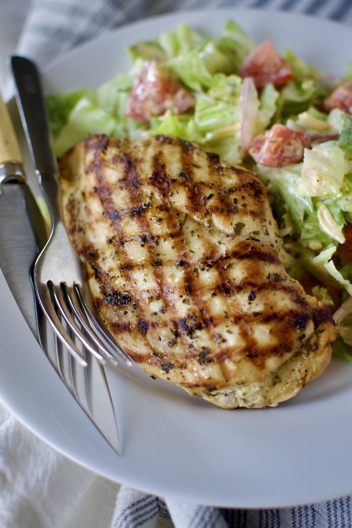Marinated chicken that has been grilled, served on a plate with a summer side salad.