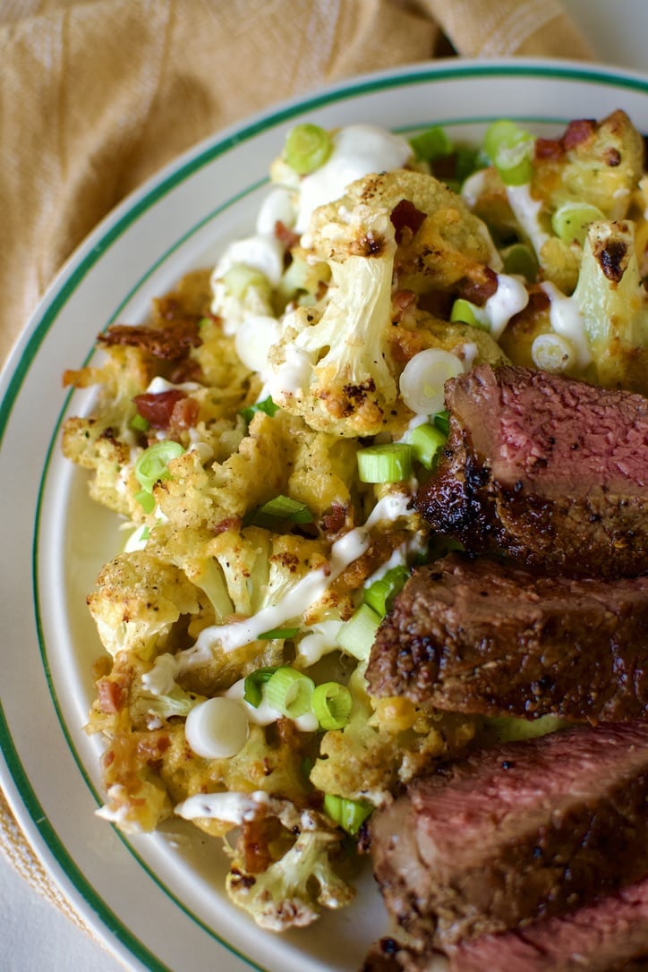 Loaded Baked Cauliflower on a plate served with a perfectly grilled steak.