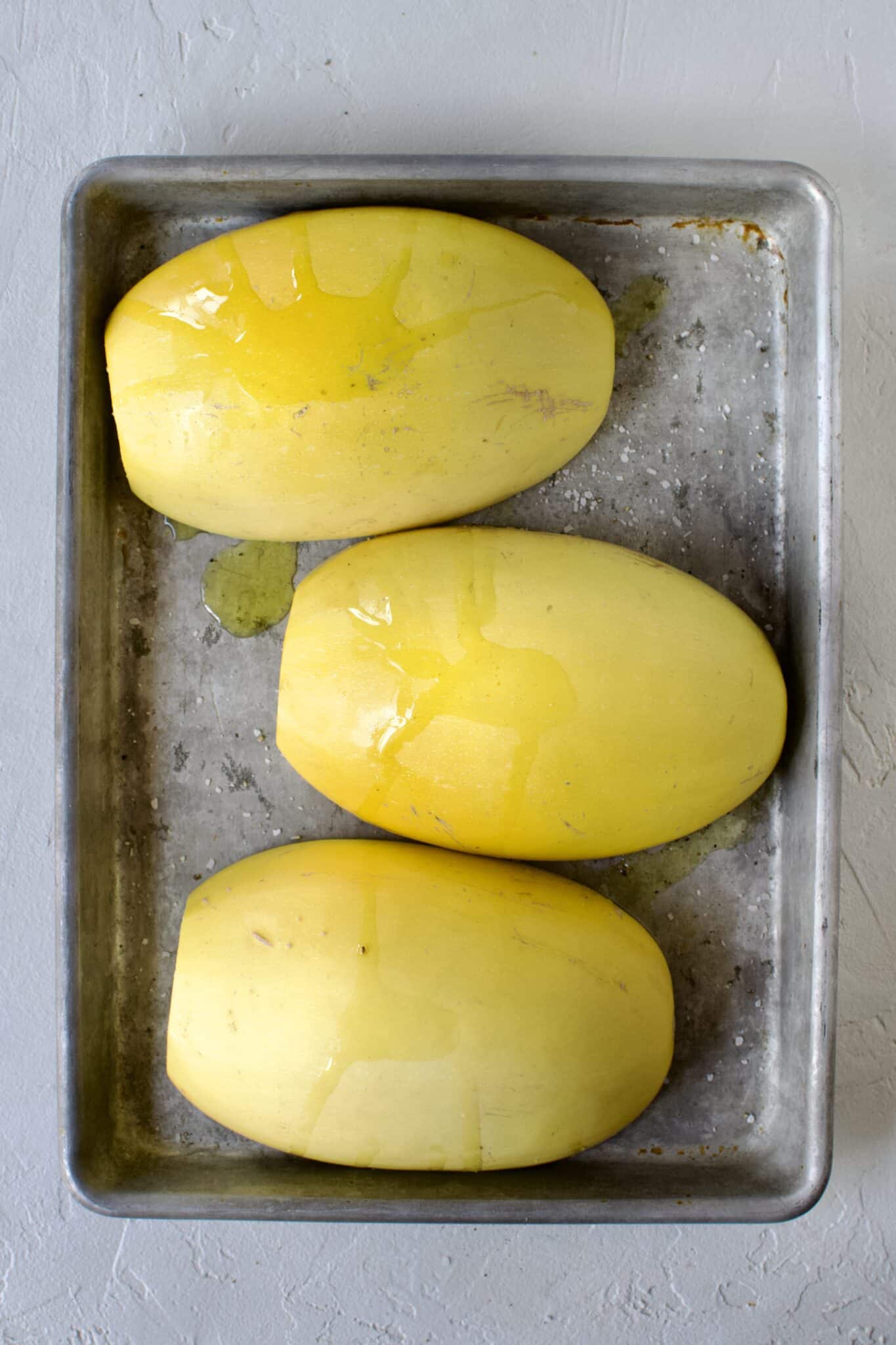 Spaghetti Squash, cut side down, seeds removed, placed on a sheet pan and seasoned with olive oil, salt, and pepper, ready to roast.