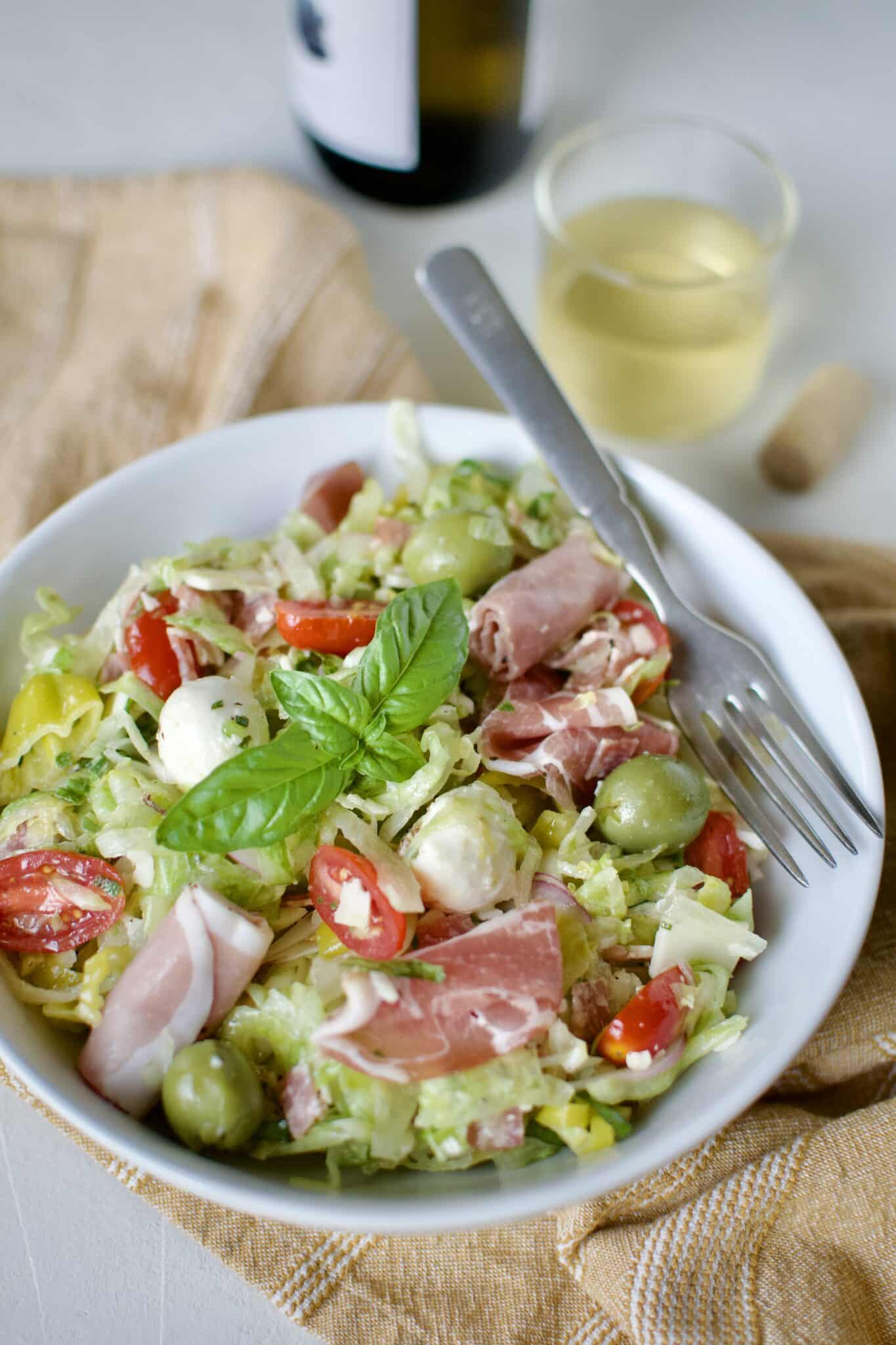 a single serving of Italian Chopped Salad in a small bowl with a glass of white wine behind it.