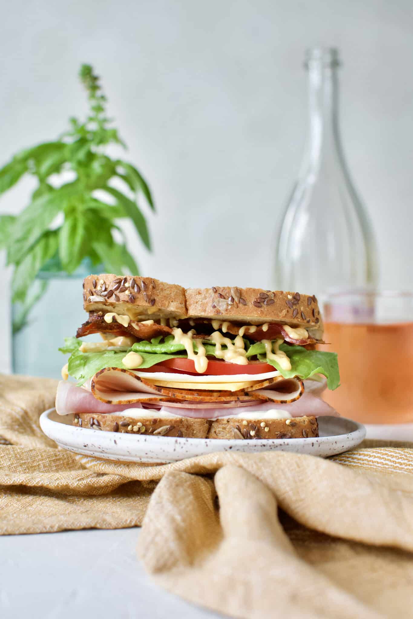 Club Sandwich Recipe on a plate served with a glass of rosé behind it.