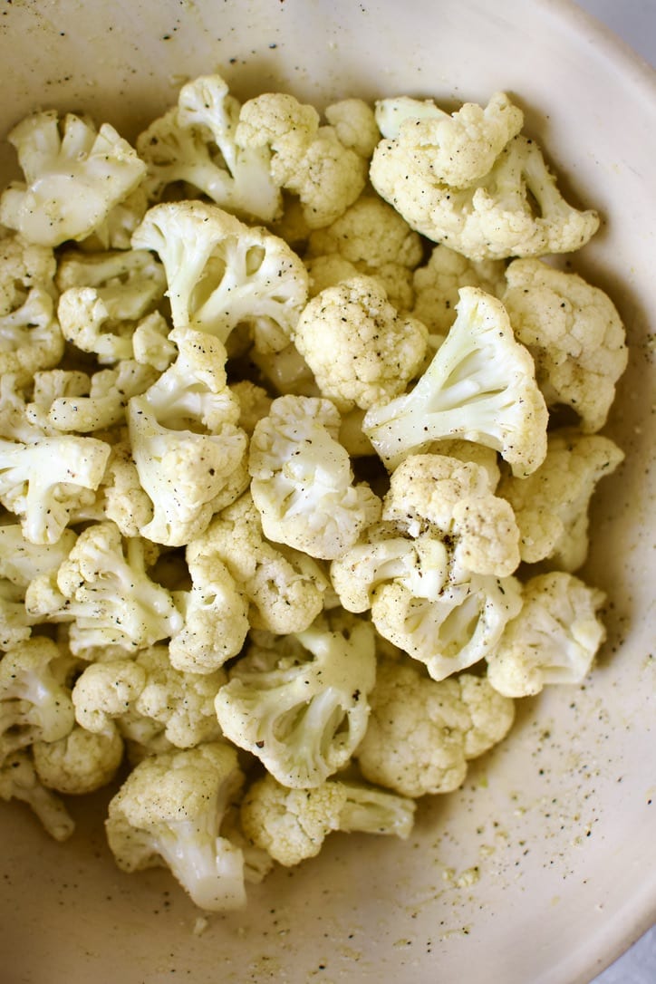 Cauliflower florets in a bowls seasoned with salt, pepper, and olive oil.