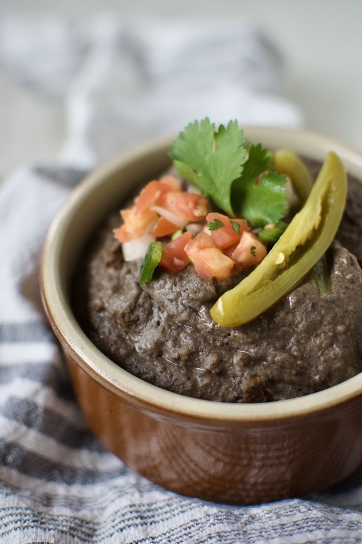 Black Bean Dip in a bowl, topped with pico de gallo, cilantro, and a slice of jalapeno.