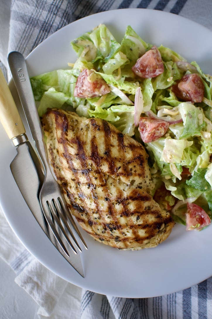 Marinated chicken that has been grilled, served on a plate with a summer side salad.