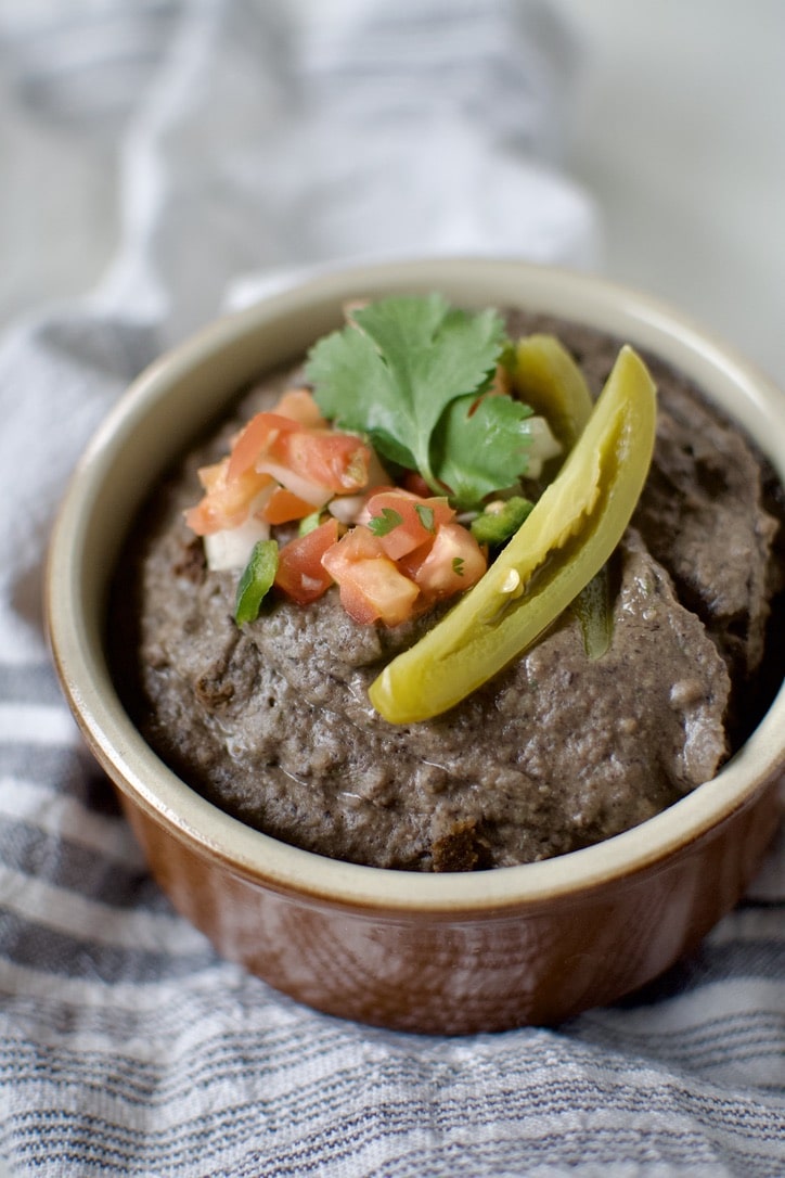 Black Bean Dip in a bowl, topped with pico de gallo, cilantro, and a slice of jalapeno.