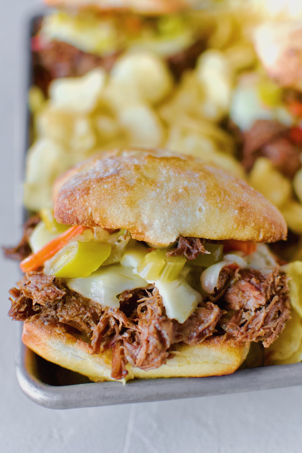 Close up shot of a single Chicago-Style Italian Beef Sandwiches served family style in a platter lined with kettle chips. Ready to be eaten!