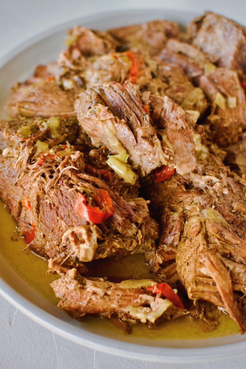 Seared beef chuck roast in a pot with onions, bell peppers, seasonings and pepperoncini after stewing 5 hours.
