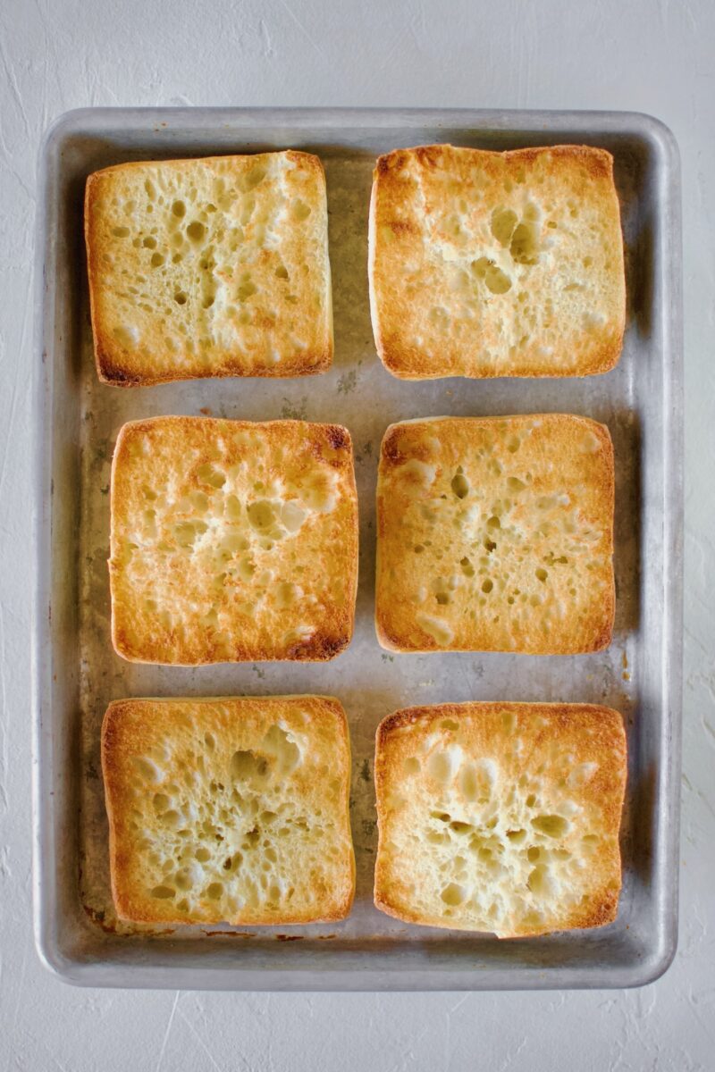 Toasted opened Ciabatta rolls on a sheet tray.