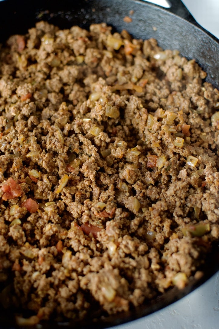 Cooked and seasoned ground beef for enchilada filling in a cast iron skillet.