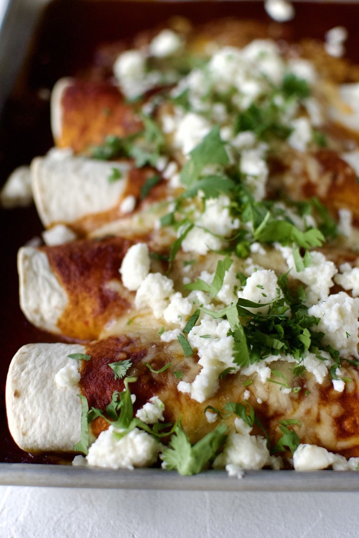 Rolled enchiladas in a baking pan, topped with red enchilada sauce, and cheese. After baking.