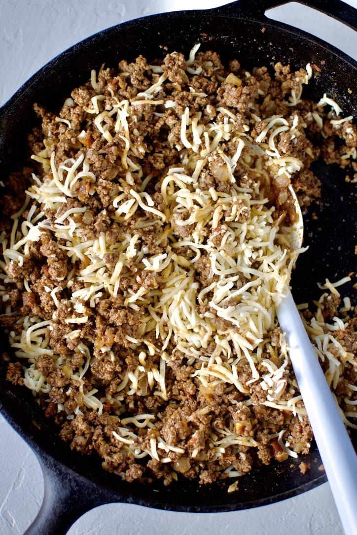 Cheese added to the enchilada filling in a cast iron skillet.