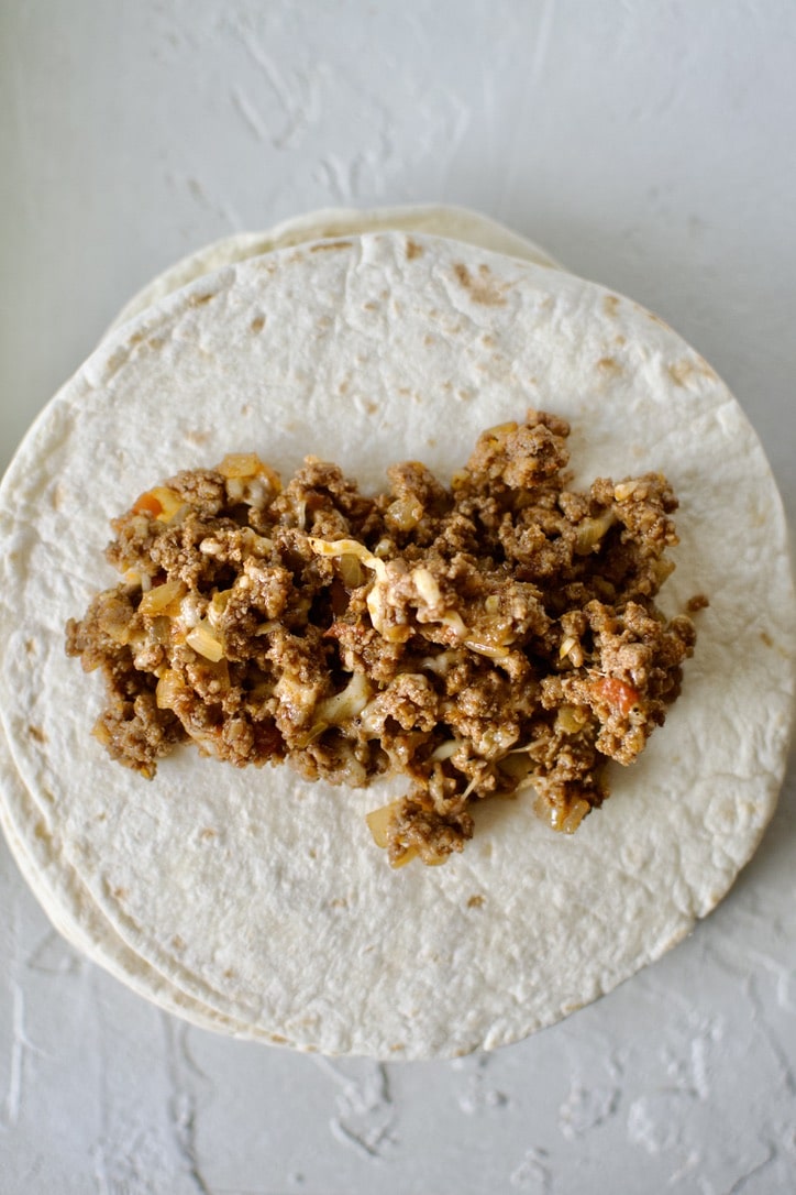 Filling the flour tortillas with the ground beef and cheese enchilada filling.