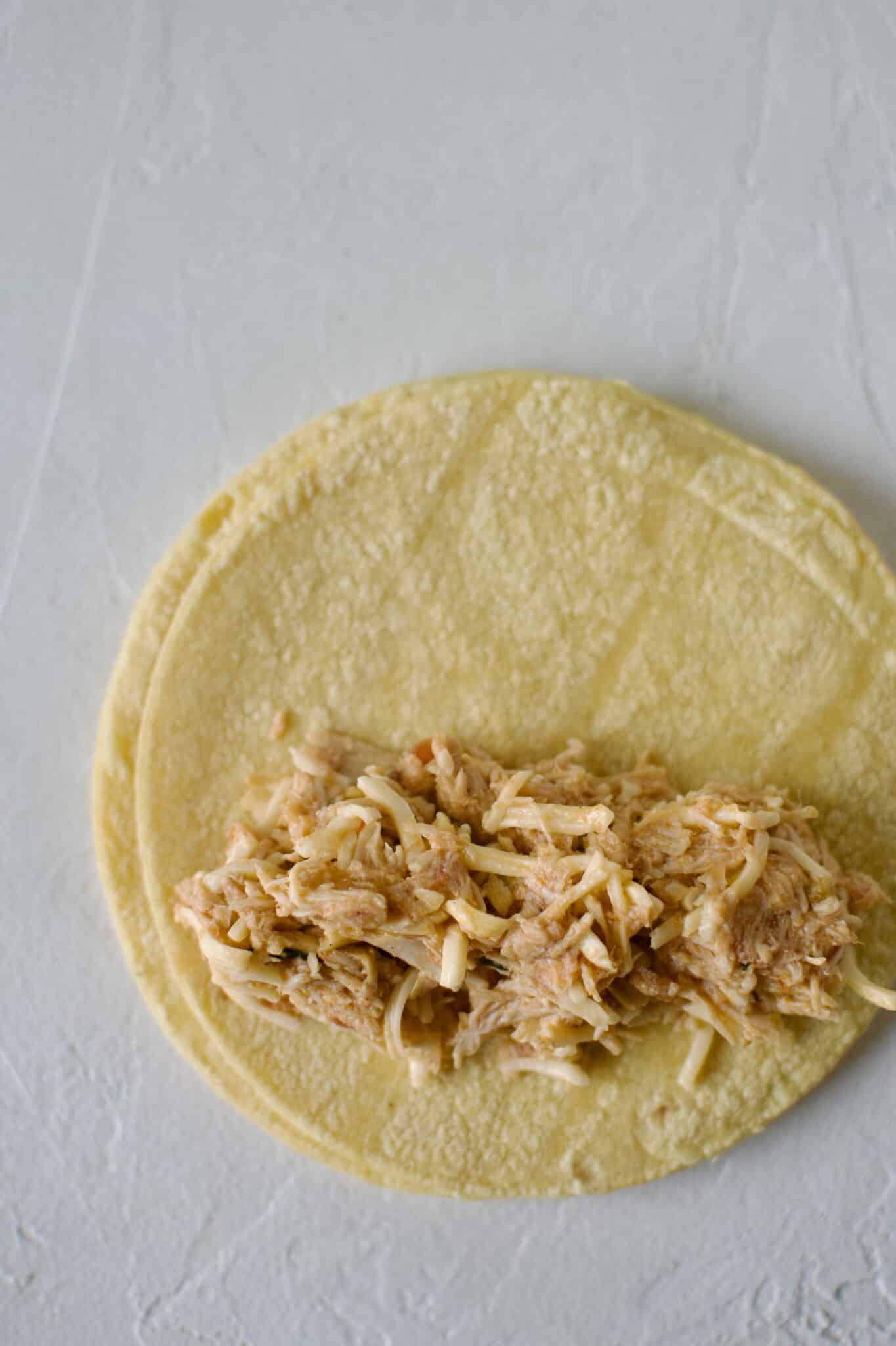 Filling a corn tortilla with mexican shredded chicken and rolling up for enchiladas.