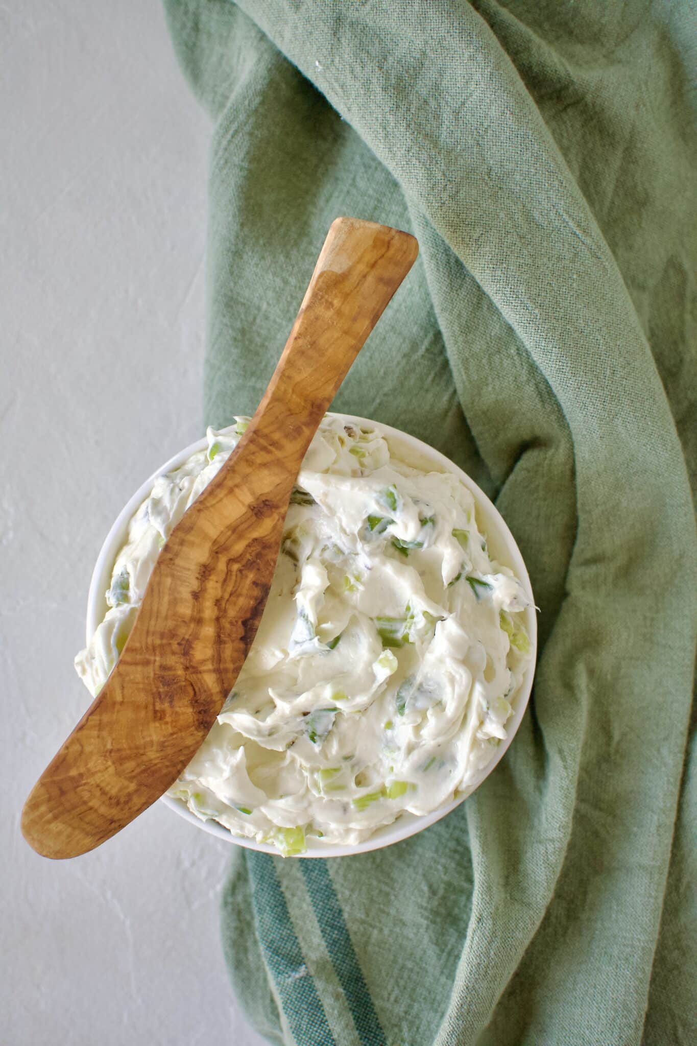 Finished scallion cream cheese in a dish ready to eat. With a wood spreading knife resting on the side.