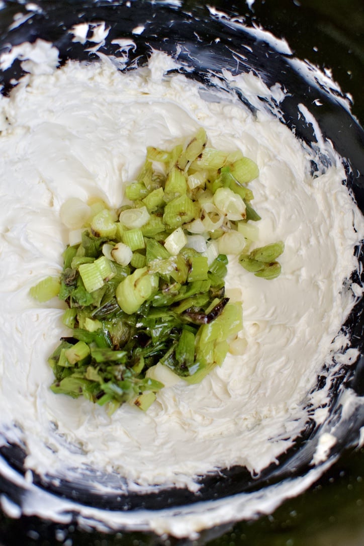 Adding the cooked and chopped scallions to the whipped cream cheese in the stand mixer bowl.
