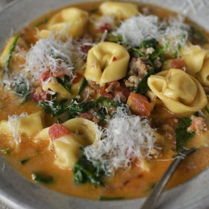 Creamy Sausage Tortellini Soup in a bowl with topped with finely shaved parmesan, ready to eat.