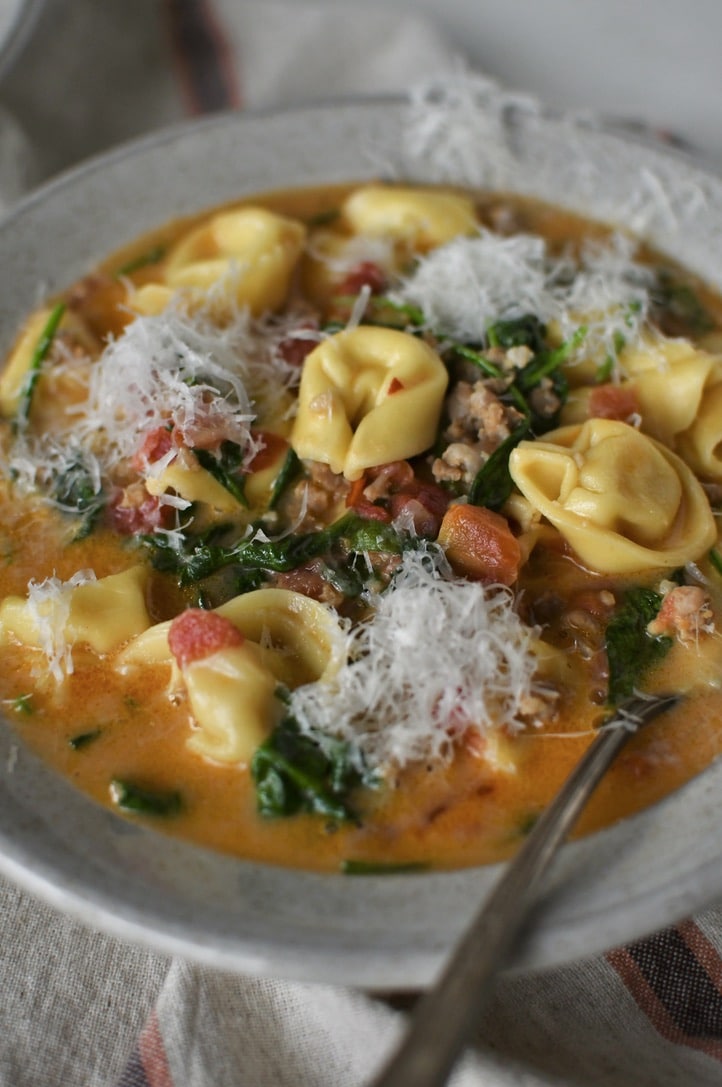 Creamy Sausage Tortellini Soup in a bowl with topped with finely shaved parmesan, ready to eat.