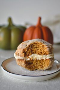 A Pumpkin Whoopie Pie on a plate with a bite taken out of it.