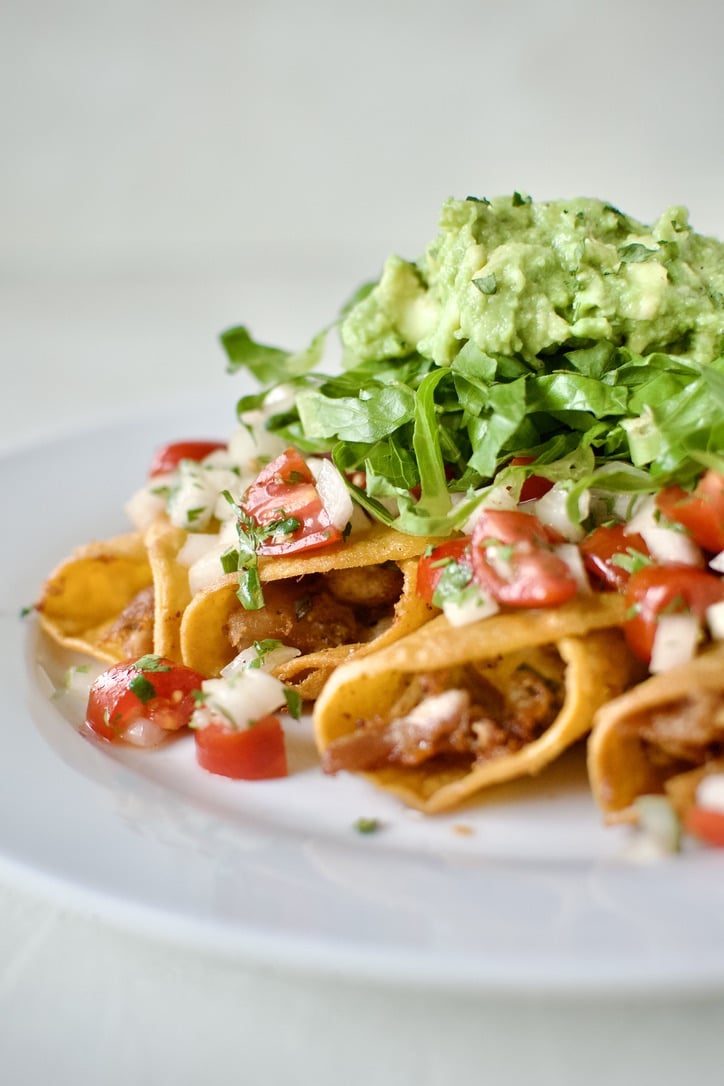 Flautas topped with pico de gallo, shredded lettuce, and avocado, ready to eat.