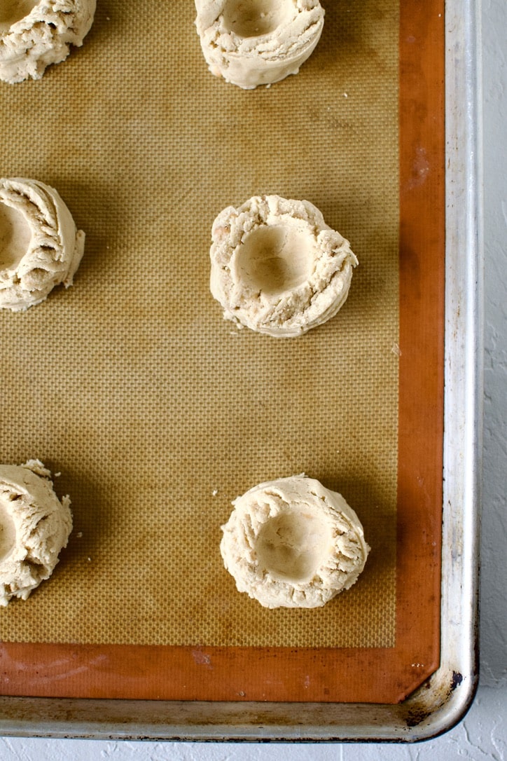 Portioned cookies on a sheet pan with an indent made in them.