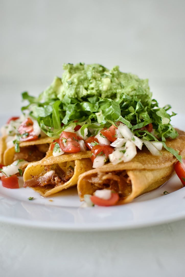 Flautas topped with pico de gallo, shredded lettuce, and avocado, ready to eat.