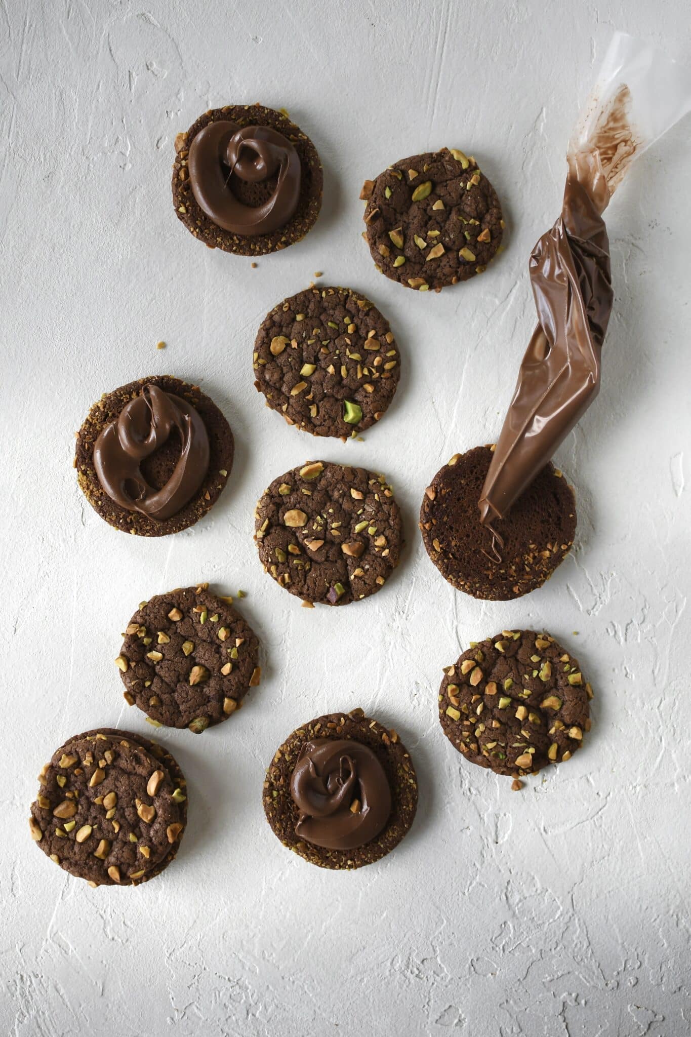 Piping nutella onto pistachio cookies before sandwiching them together.