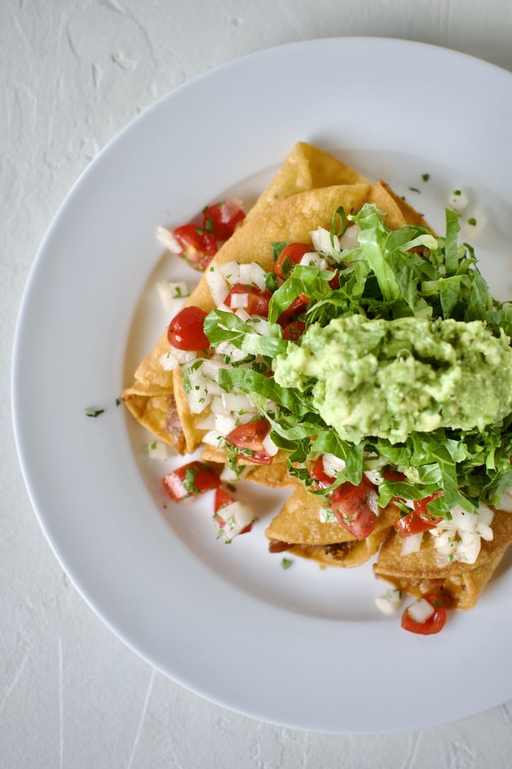 Flautas topped with pico de gallo, shredded lettuce, and avocado, ready to eat.